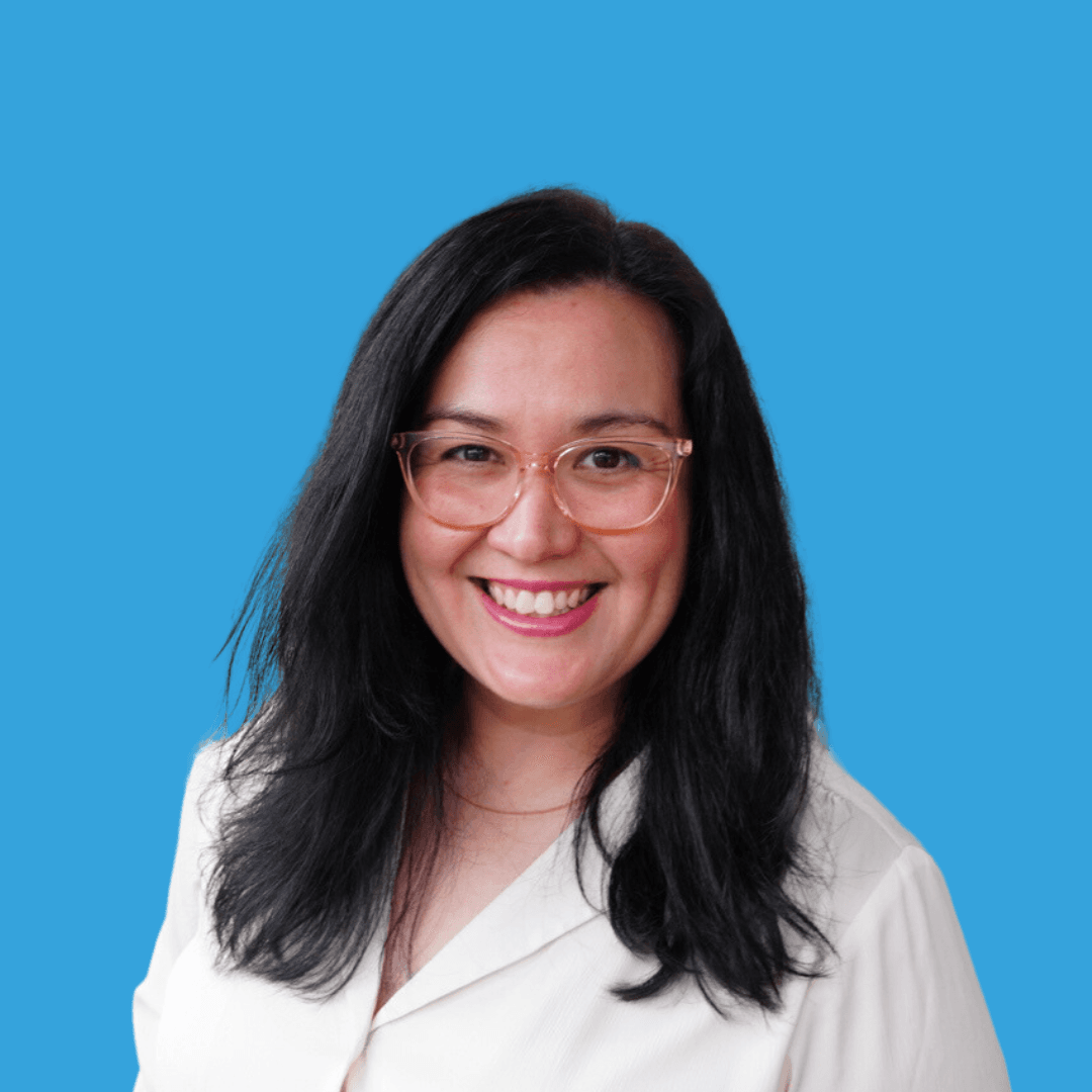 A woman in glasses smiling at the camera on a blue background