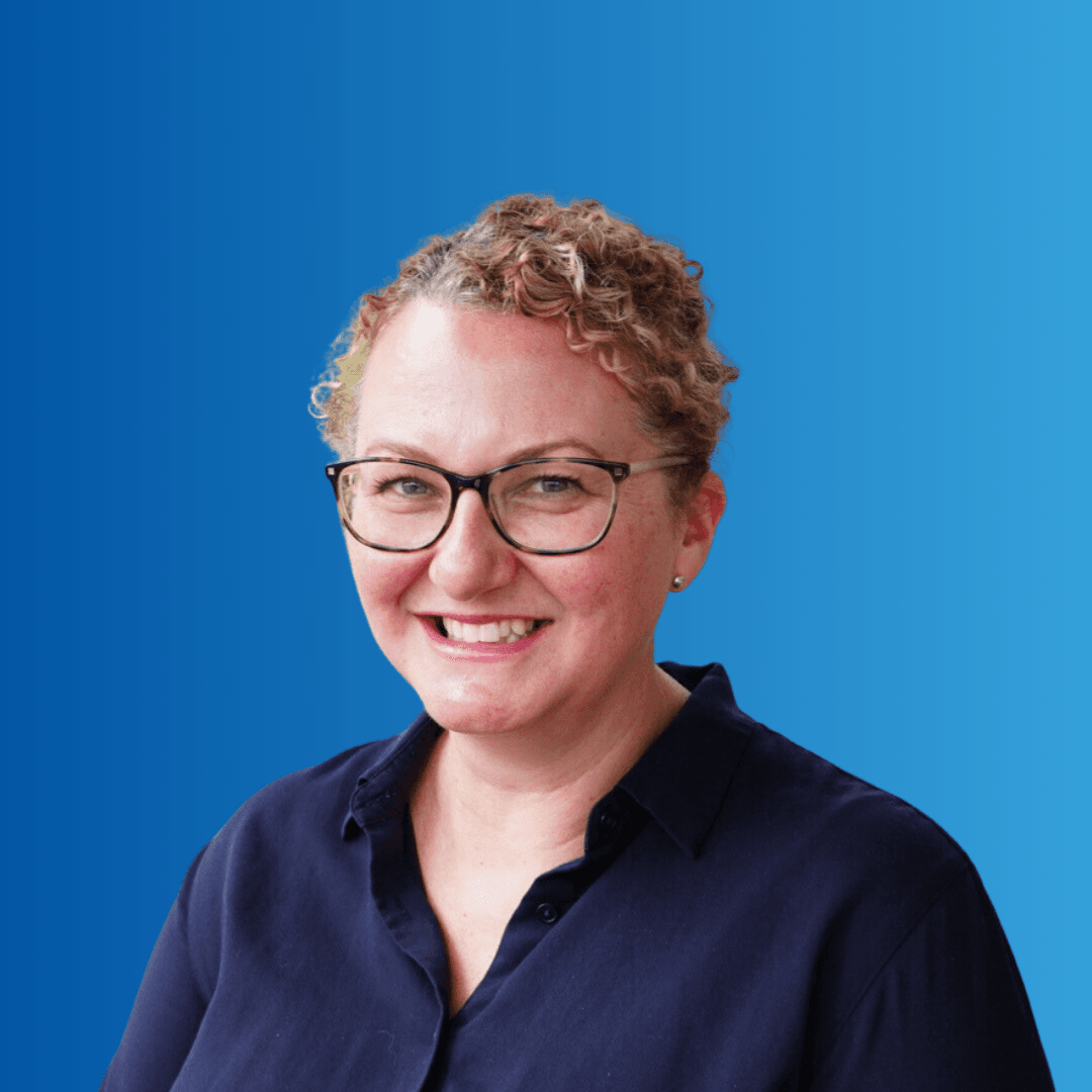 A woman in glasses smiling at the camera on a blue background